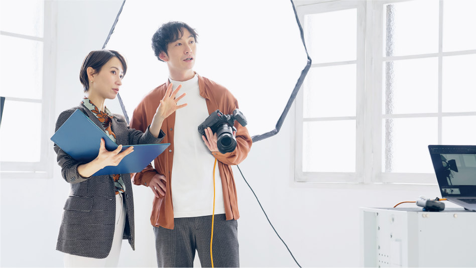 撮影現場でカメラを持つ男性と男性に指示を出す女性